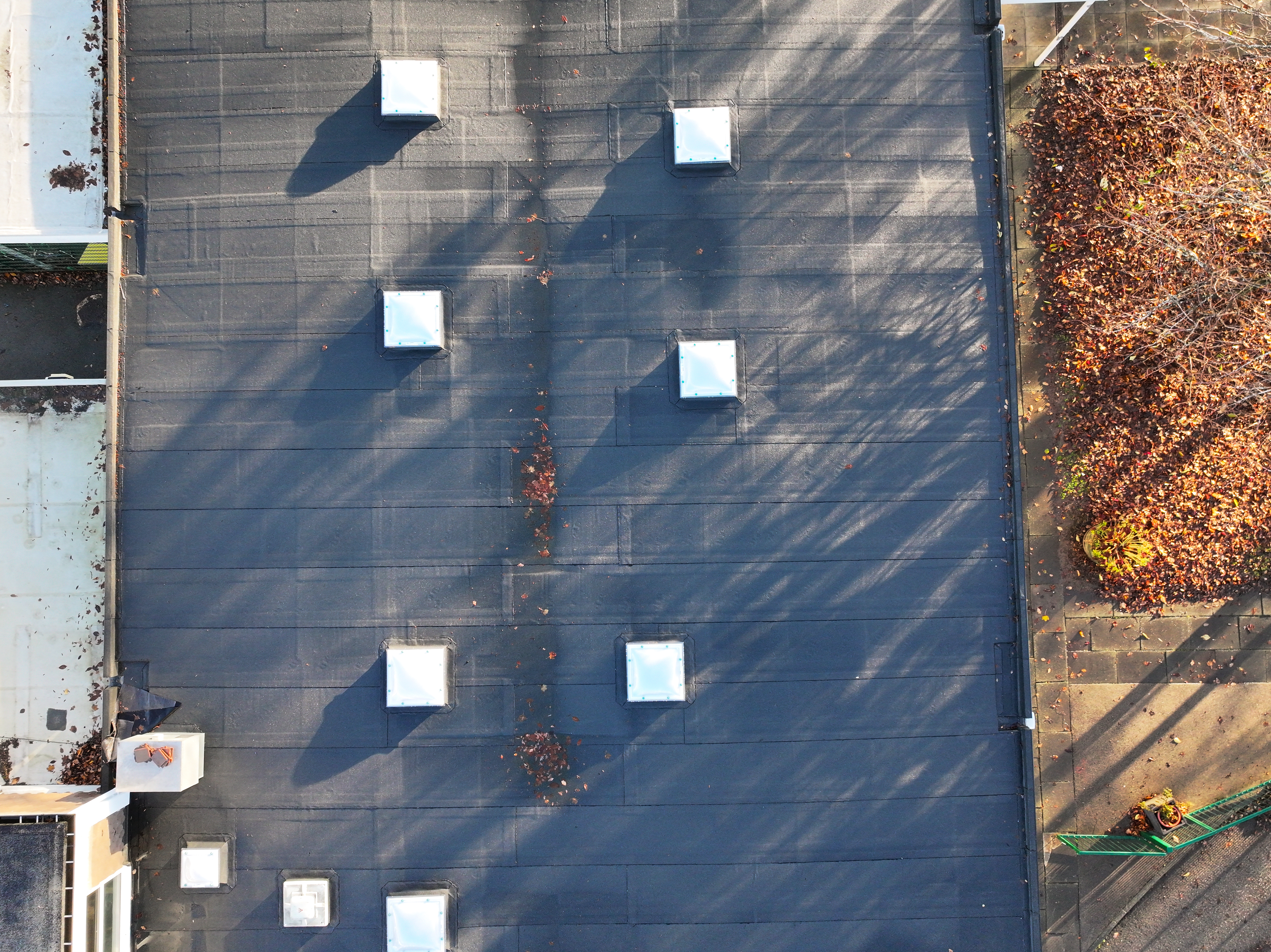 Aerial view of flat roof with nine white square vents arranged in grid pattern, diagonal shadows across grey surface.