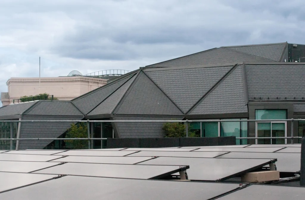 Grey angular roof structure with green window frames and geometric metal cladding under cloudy sky.