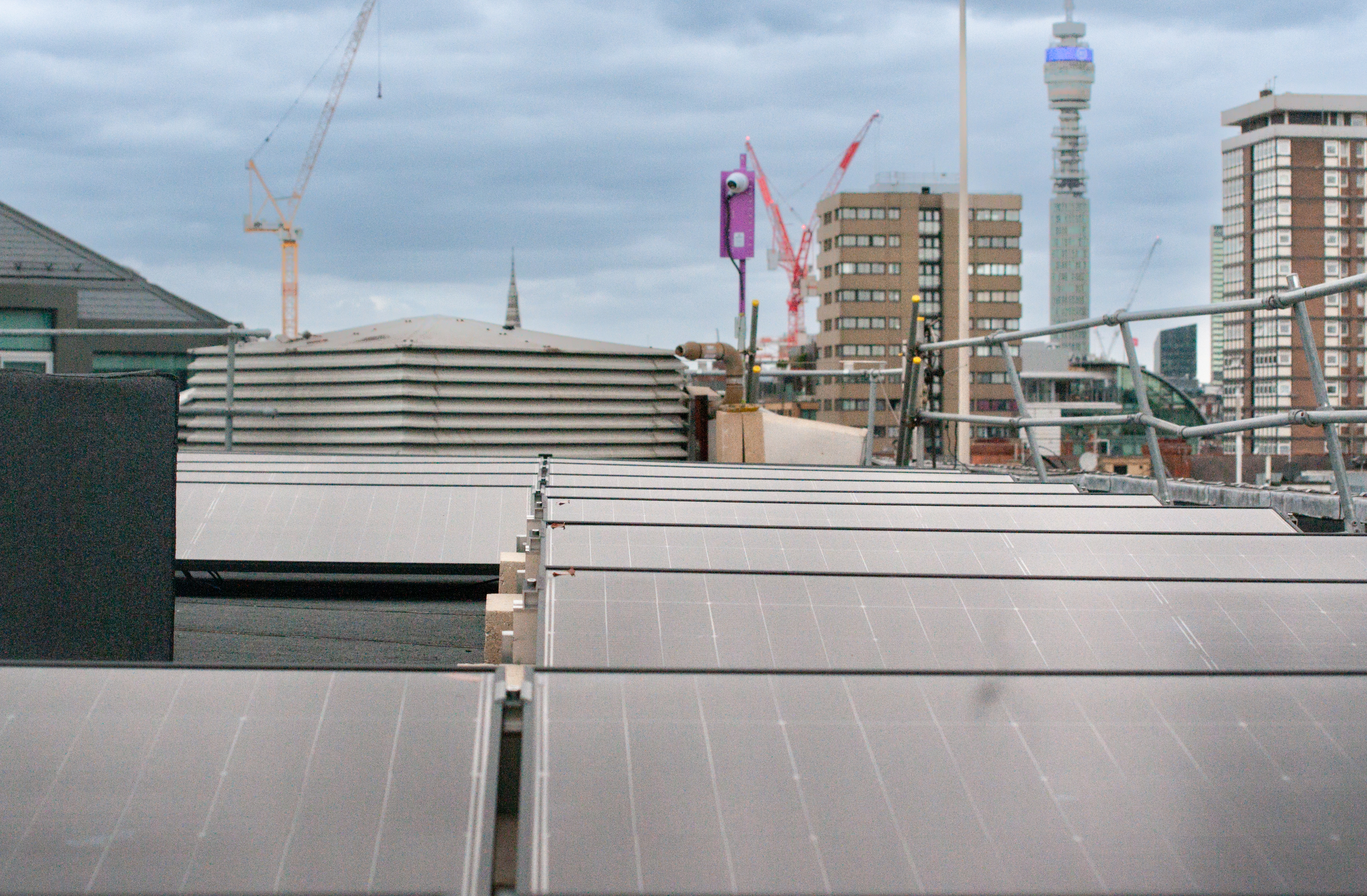Urban rooftop view with metal ventilation ducts in foreground, construction cranes and high-rise buildings in background.