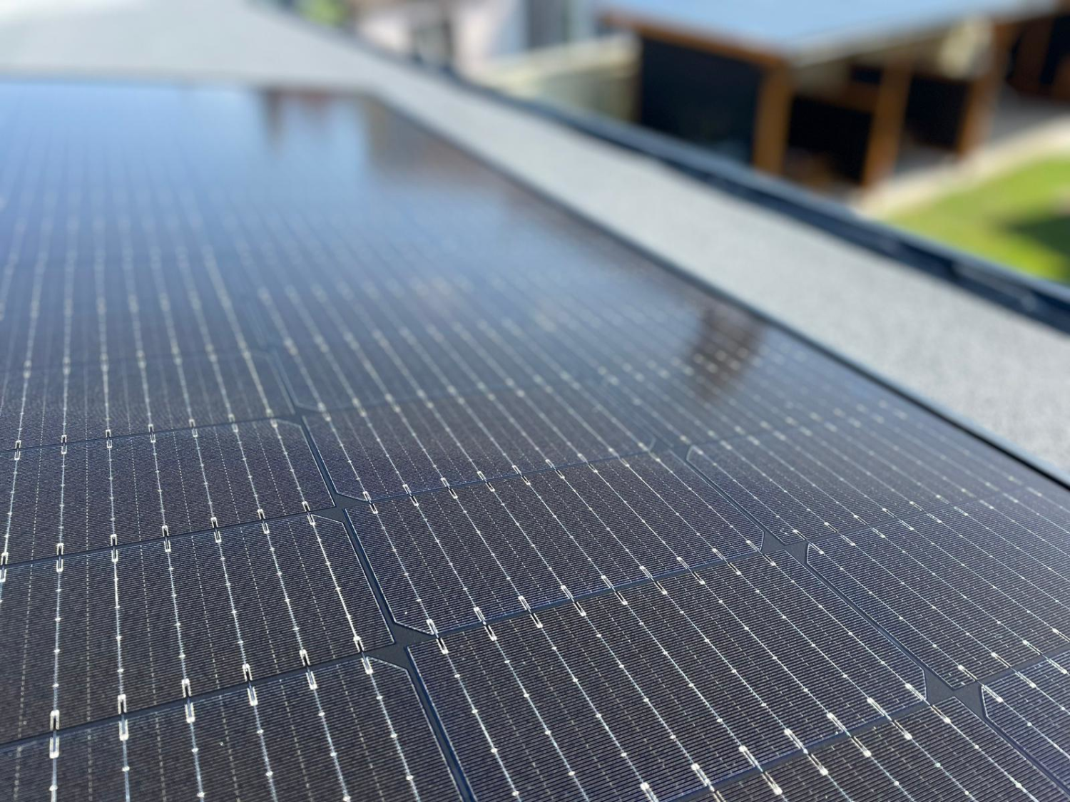 Dark blue solar panels with grid pattern of white lines on rooftop, blurred building in background.