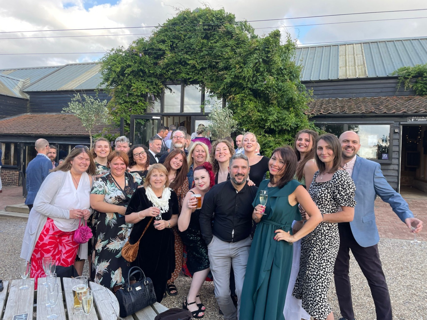 Large group of people in formal and semi-formal attire posing together in courtyard with buildings and large tree in background.