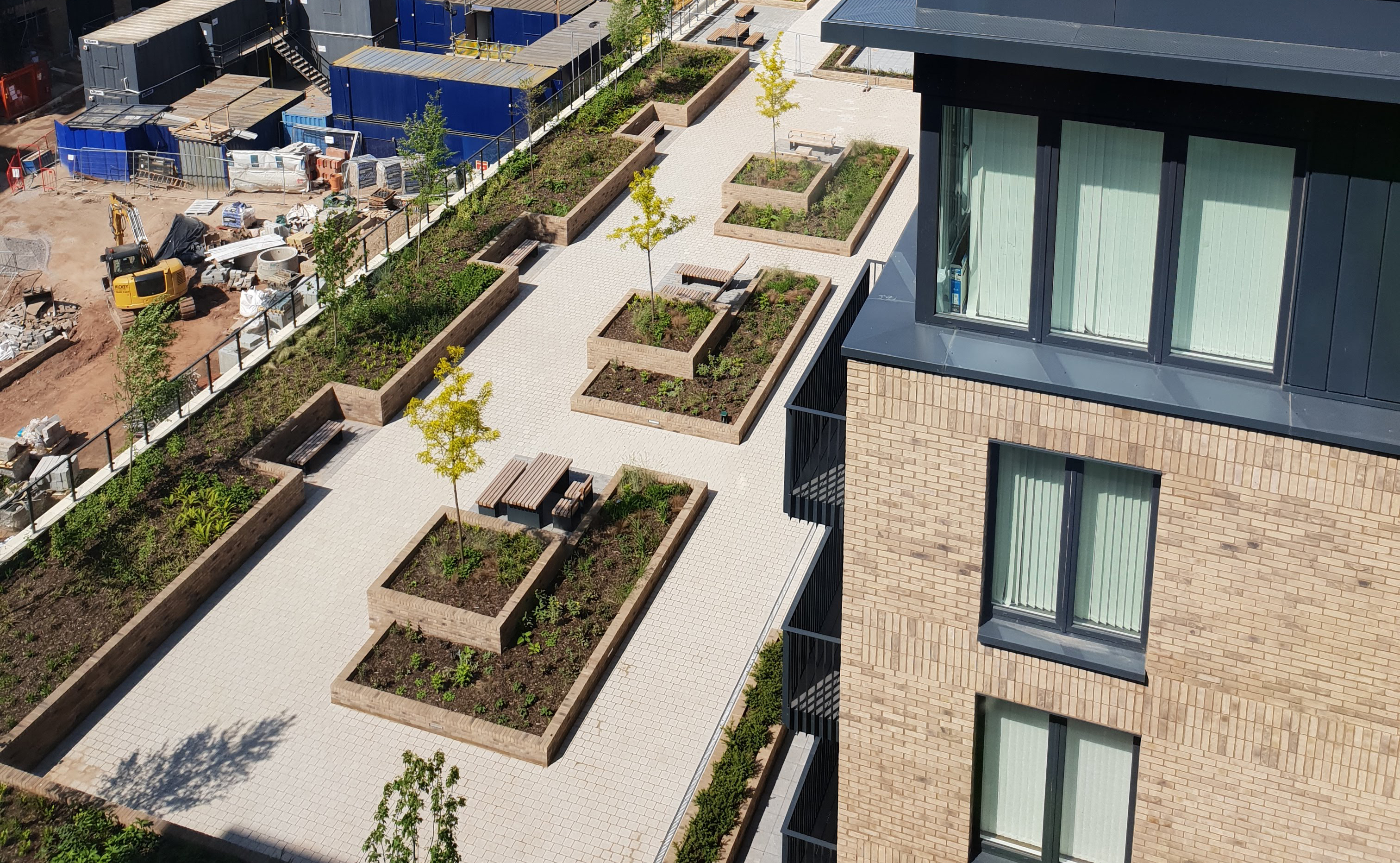 Aerial view of modern residential development with rectangular garden plots, concrete pathways, and brick buildings with blue trim.