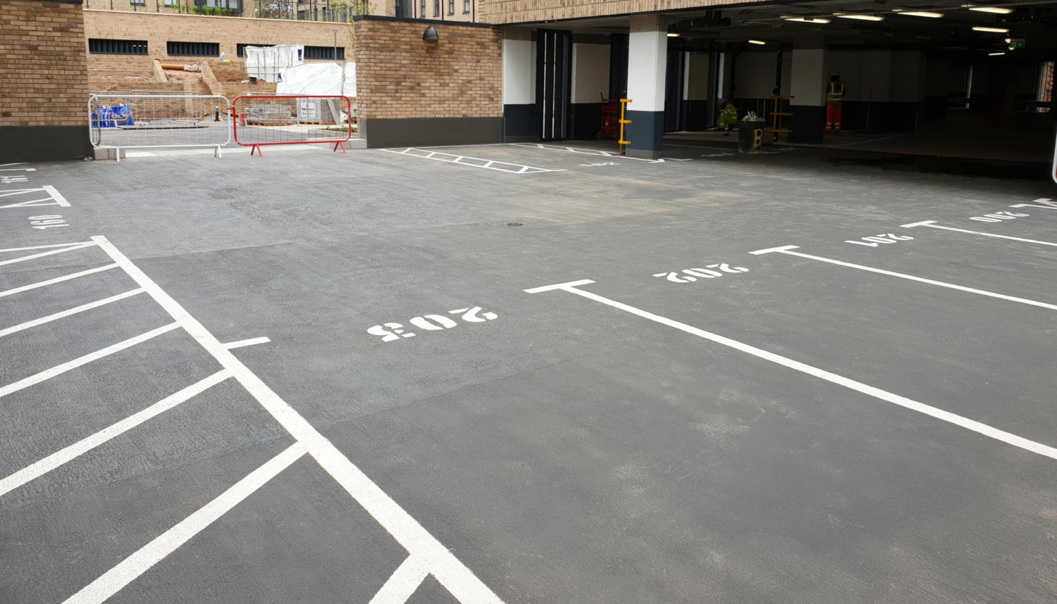 Multi-storey car park with white painted bay markings on grey concrete floor, brick building with glass entrance visible.