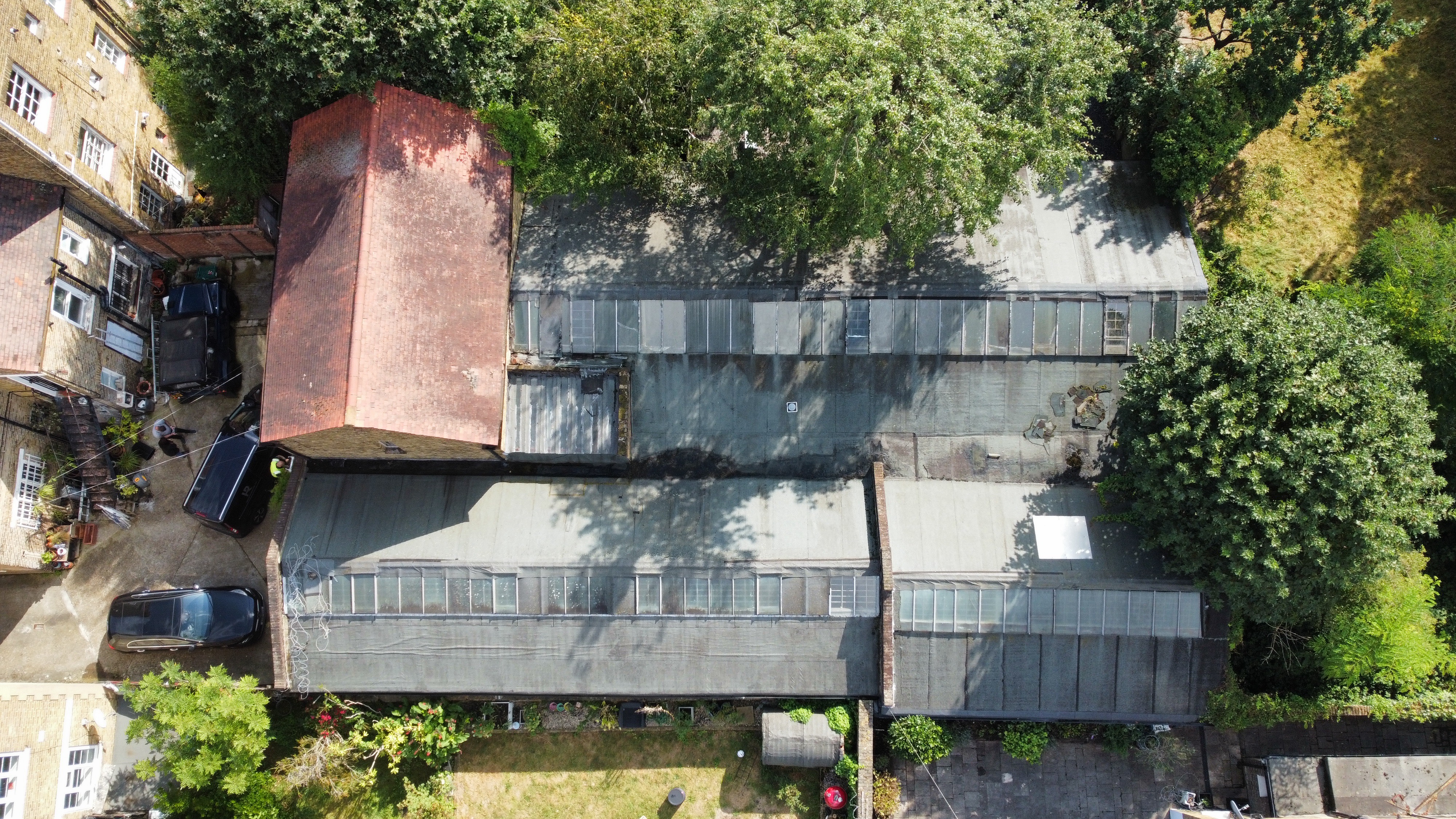 Aerial view of modern single-storey building with flat grey roof surrounded by green trees and neighbouring houses with gardens.