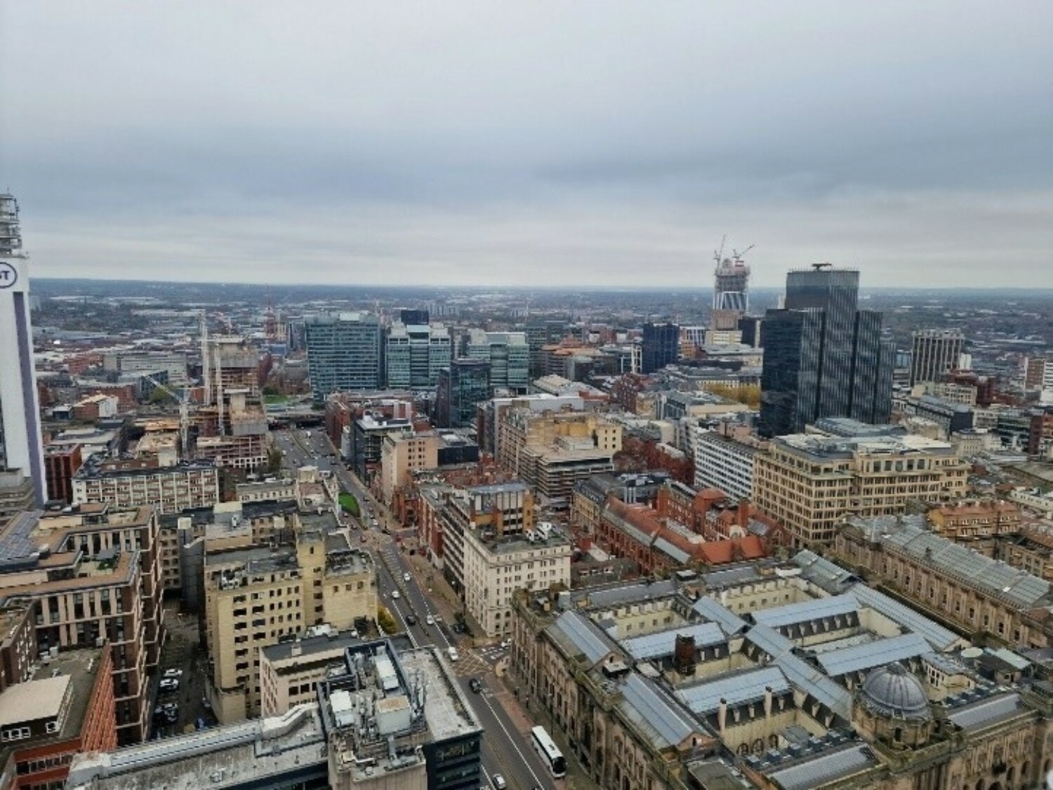 Aerial view of city centre with mix of modern glass towers and older brick buildings under overcast grey sky.