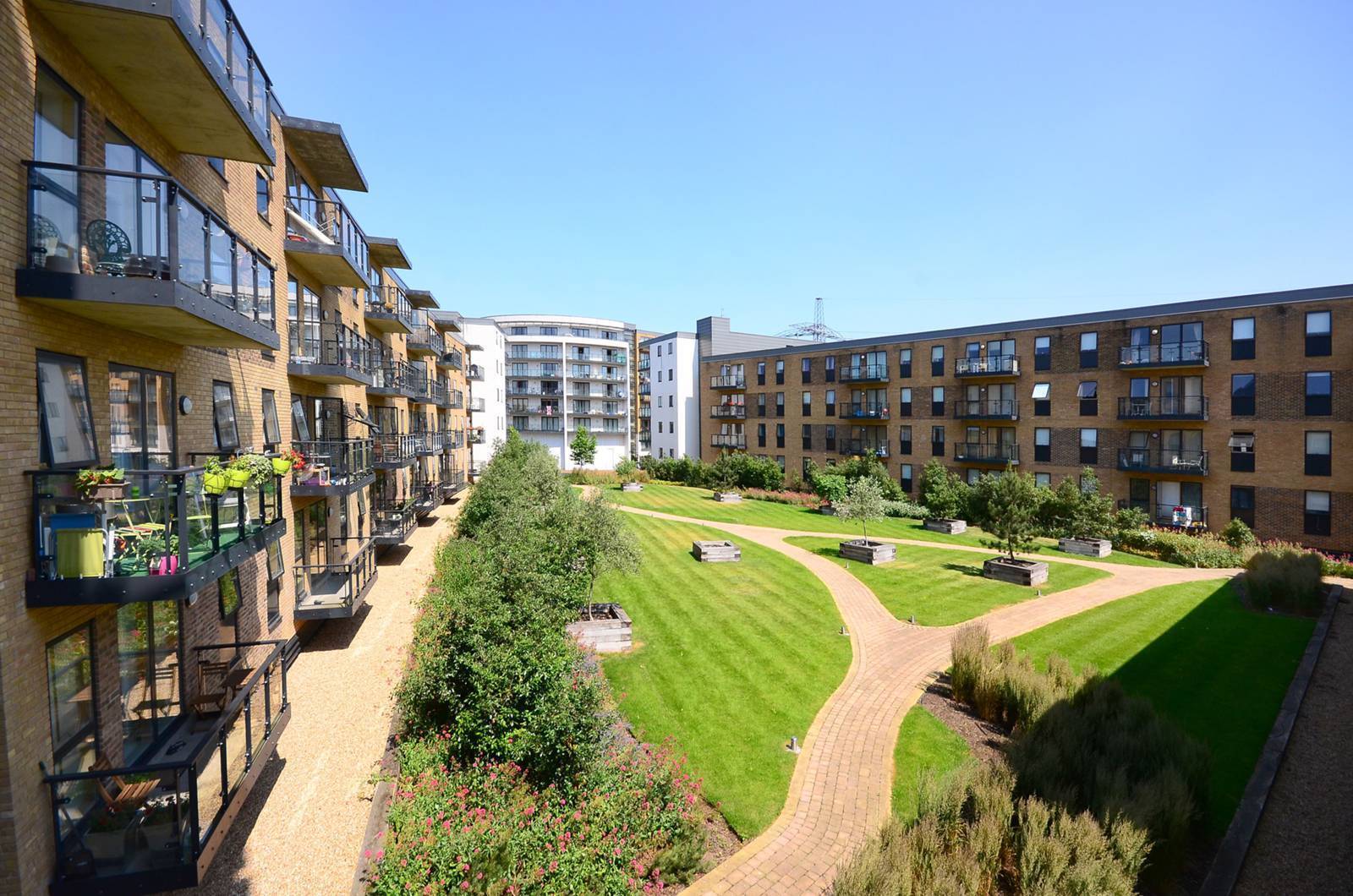 Modern residential development with brown brick flats surrounding central green space featuring curved pathways and manicured lawn.