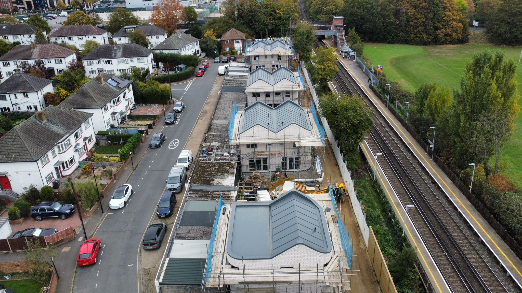 Aerial view of construction site with grey-roofed buildings under development, surrounded by residential houses and railway line