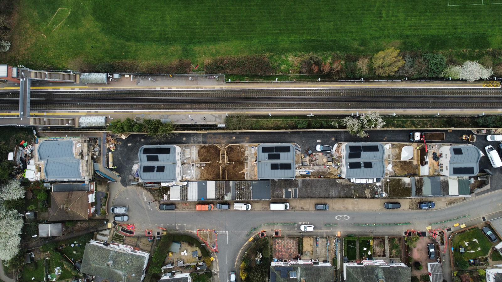 Aerial view of residential street with houses, gardens, and railway line running horizontally across top of image