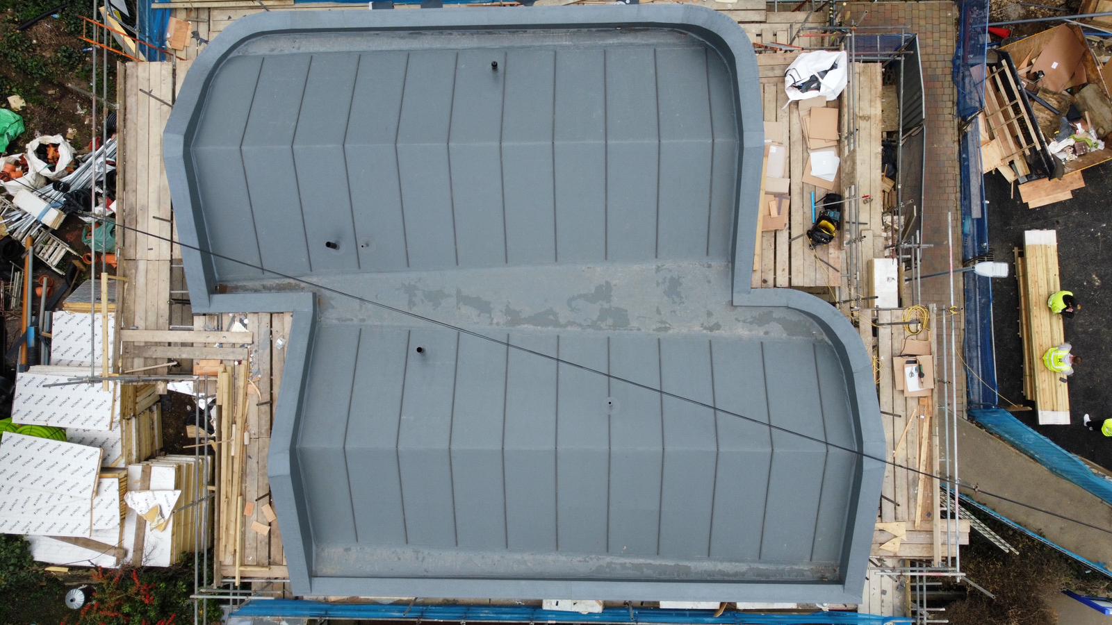 Aerial view of two large rectangular pools with green-blue water, surrounded by concrete decking and construction materials