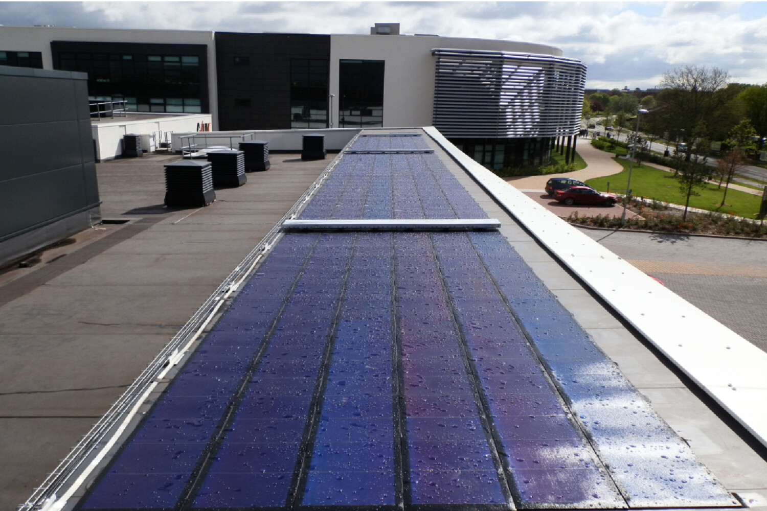 Modern building with blue solar panels on flat roof, grey concrete structure with glass windows in background under cloudy sky.