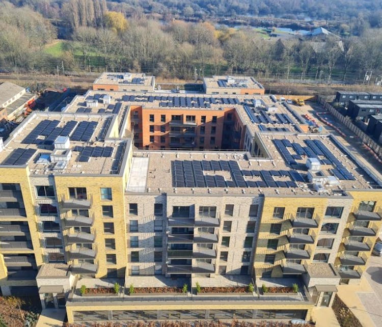 Aerial view of modern residential development with yellow and orange brick buildings arranged around central courtyard, surrounded by trees.