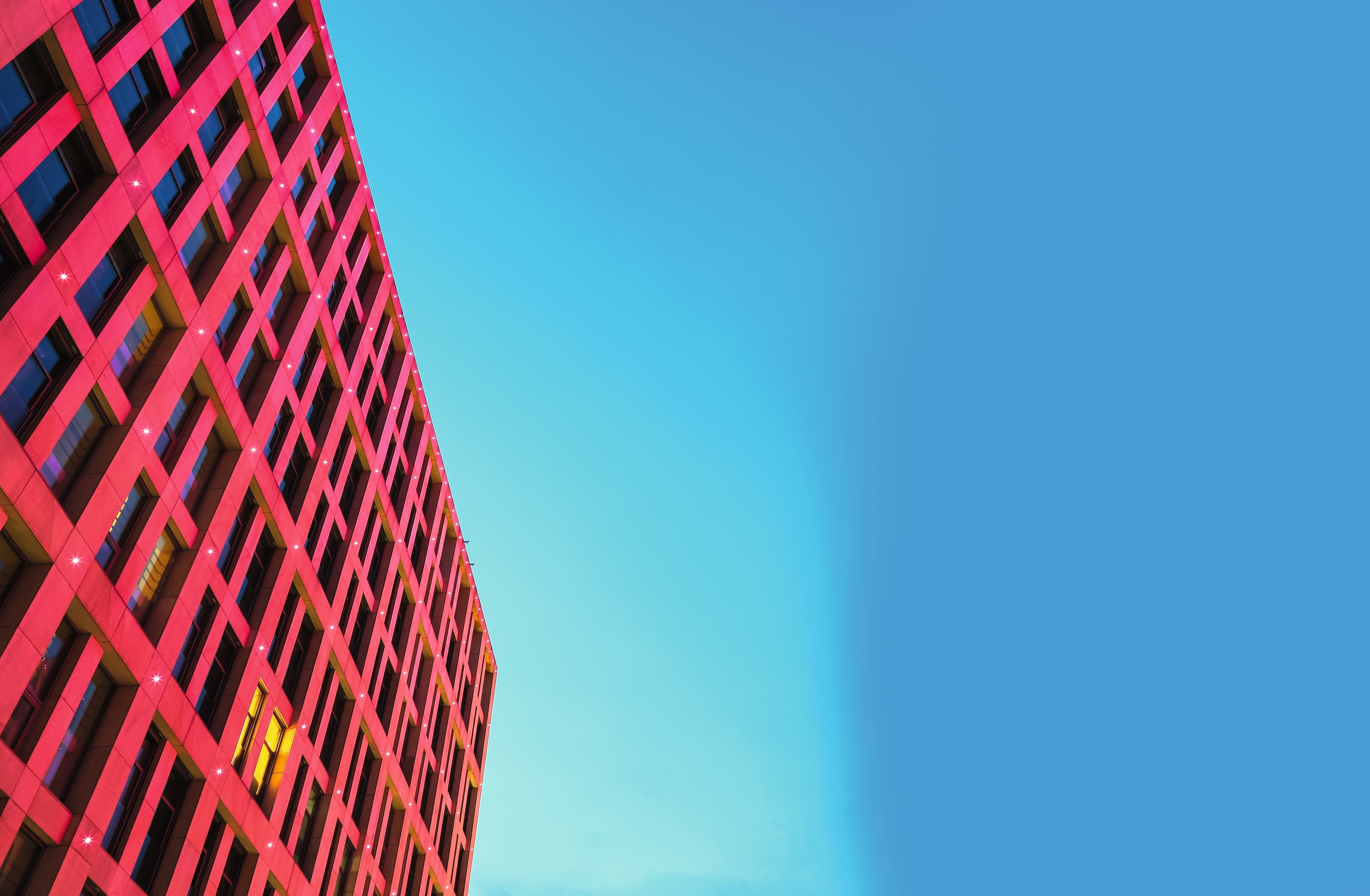 Red geometric building with grid pattern shot from below against bright blue sky with white clouds.