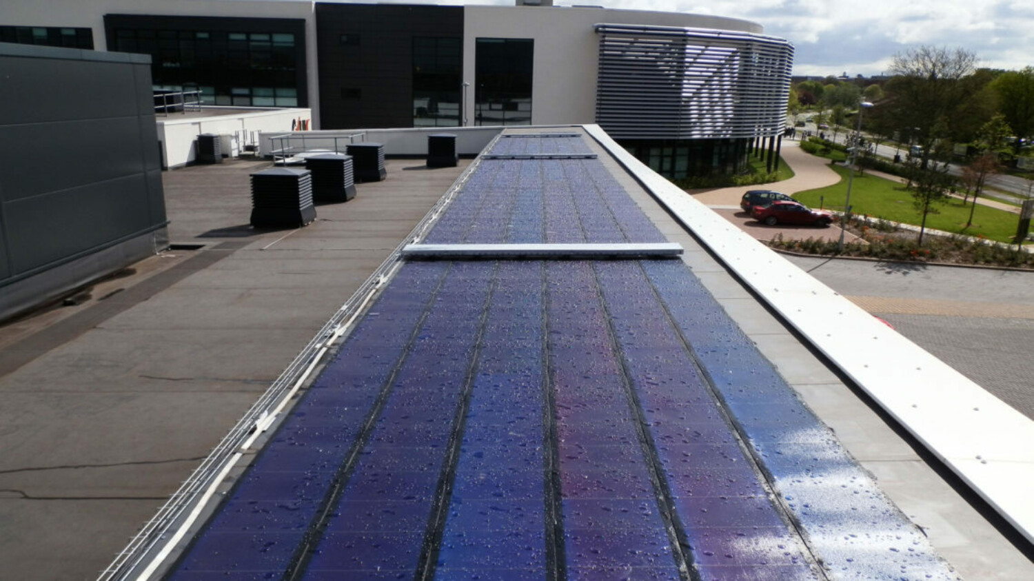 Solar panels installed on flat rooftop of modern building with grey concrete surfaces and HVAC equipment visible.