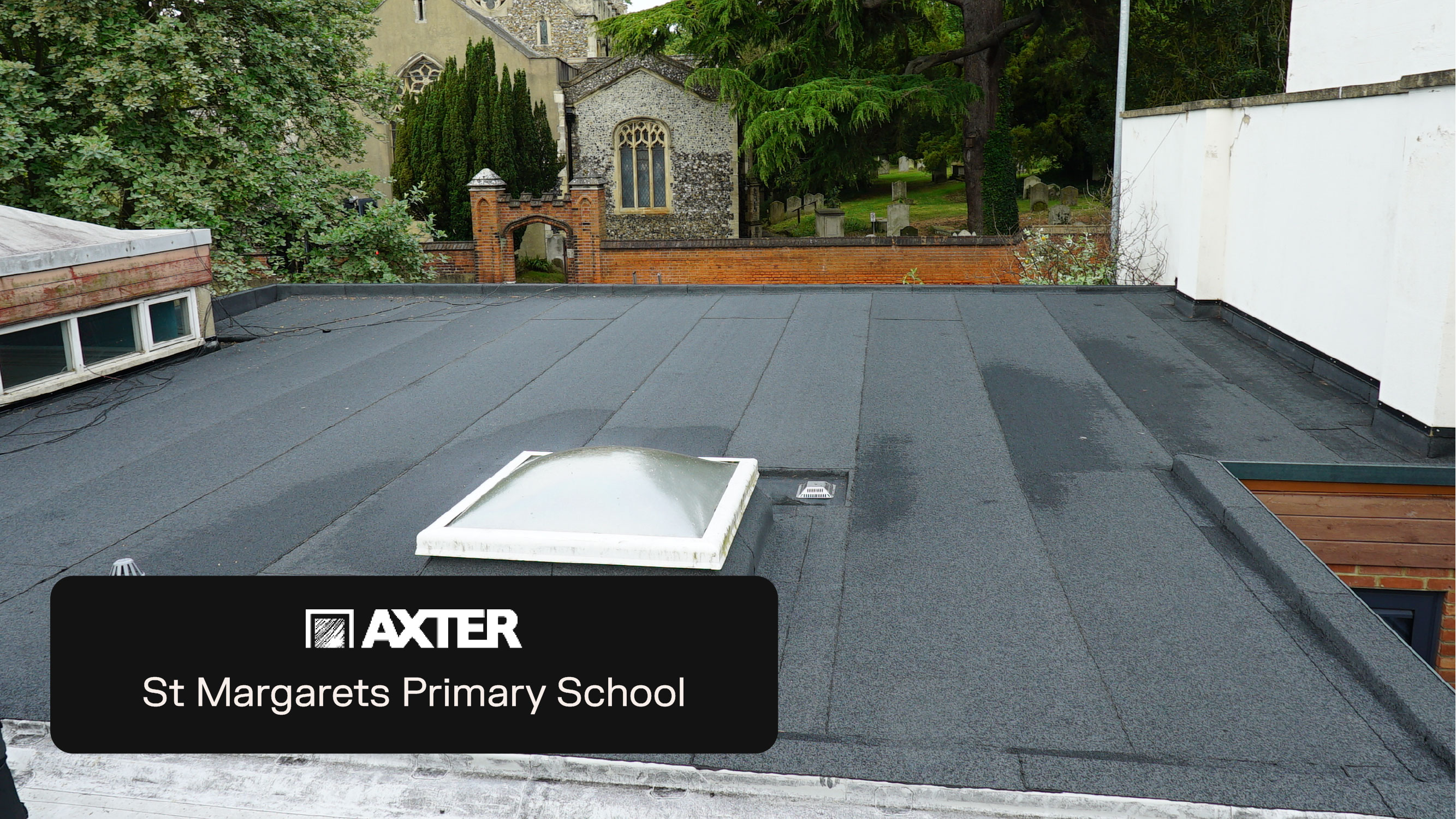 Grey flat roof with white rooflight, black Axter signage for St Margarets Primary School, church building and trees visible beyond.