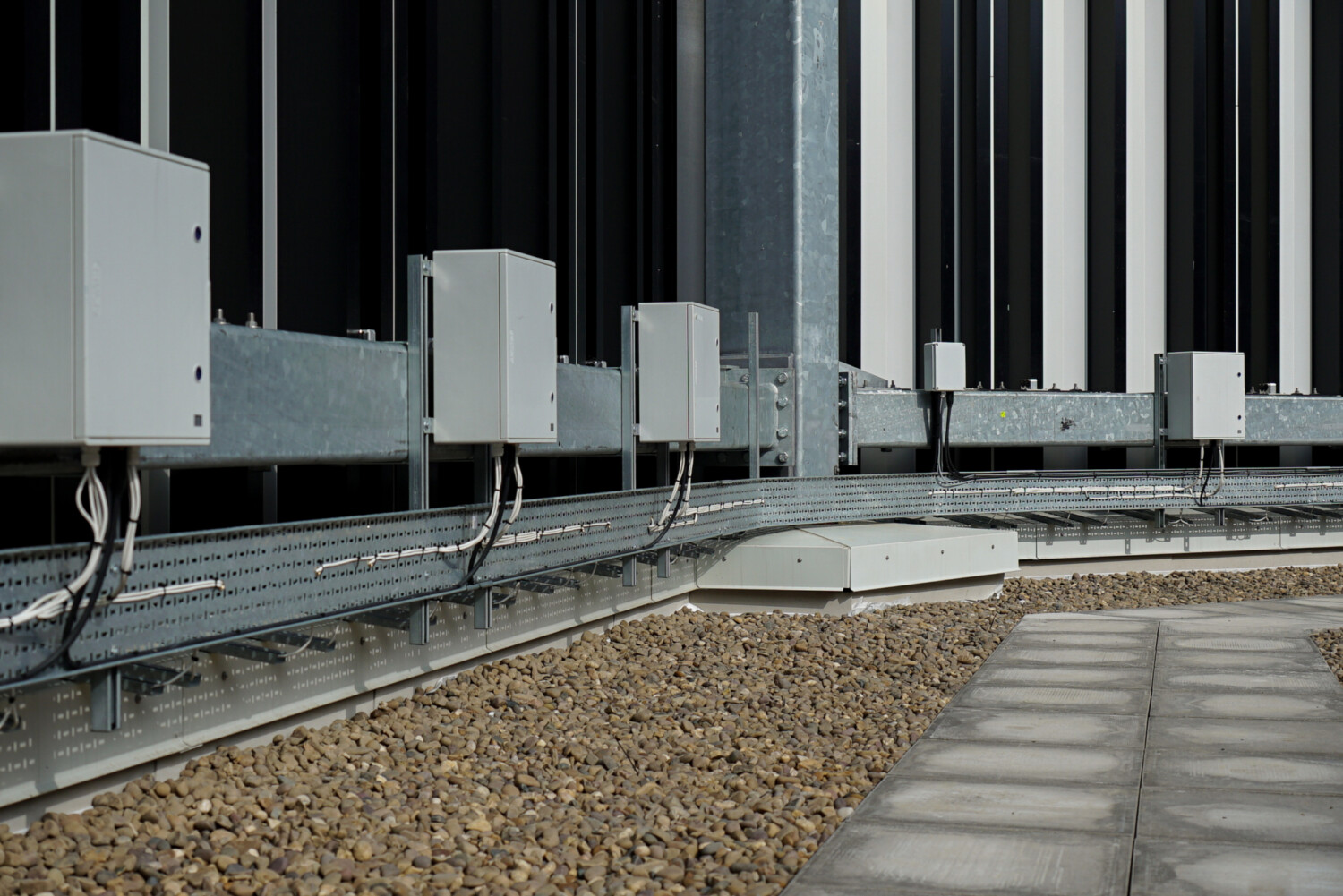 White HVAC units on concrete rooftop with metal railings, gravel surface, and vertical building facade in background.