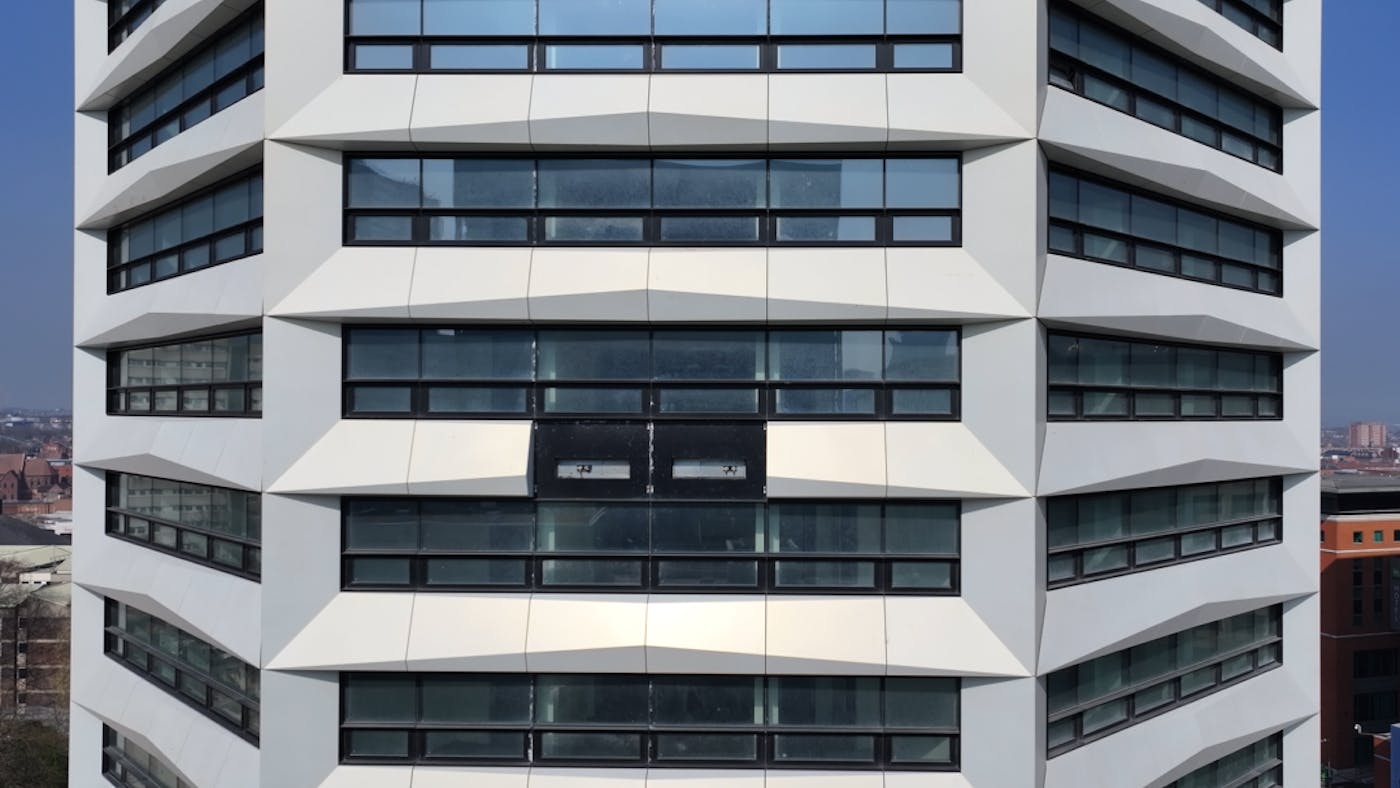 Modern white concrete building with horizontal bands of dark glass windows across multiple floors in geometric pattern.