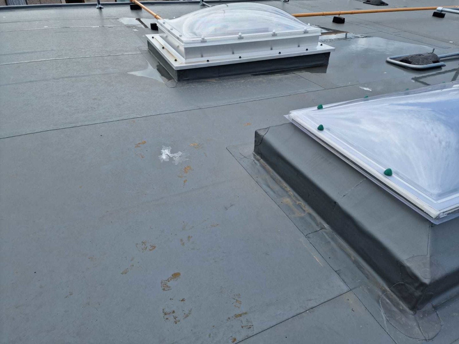 Grey flat roof with three rectangular skylights featuring clear domed tops and white frames mounted on raised bases.