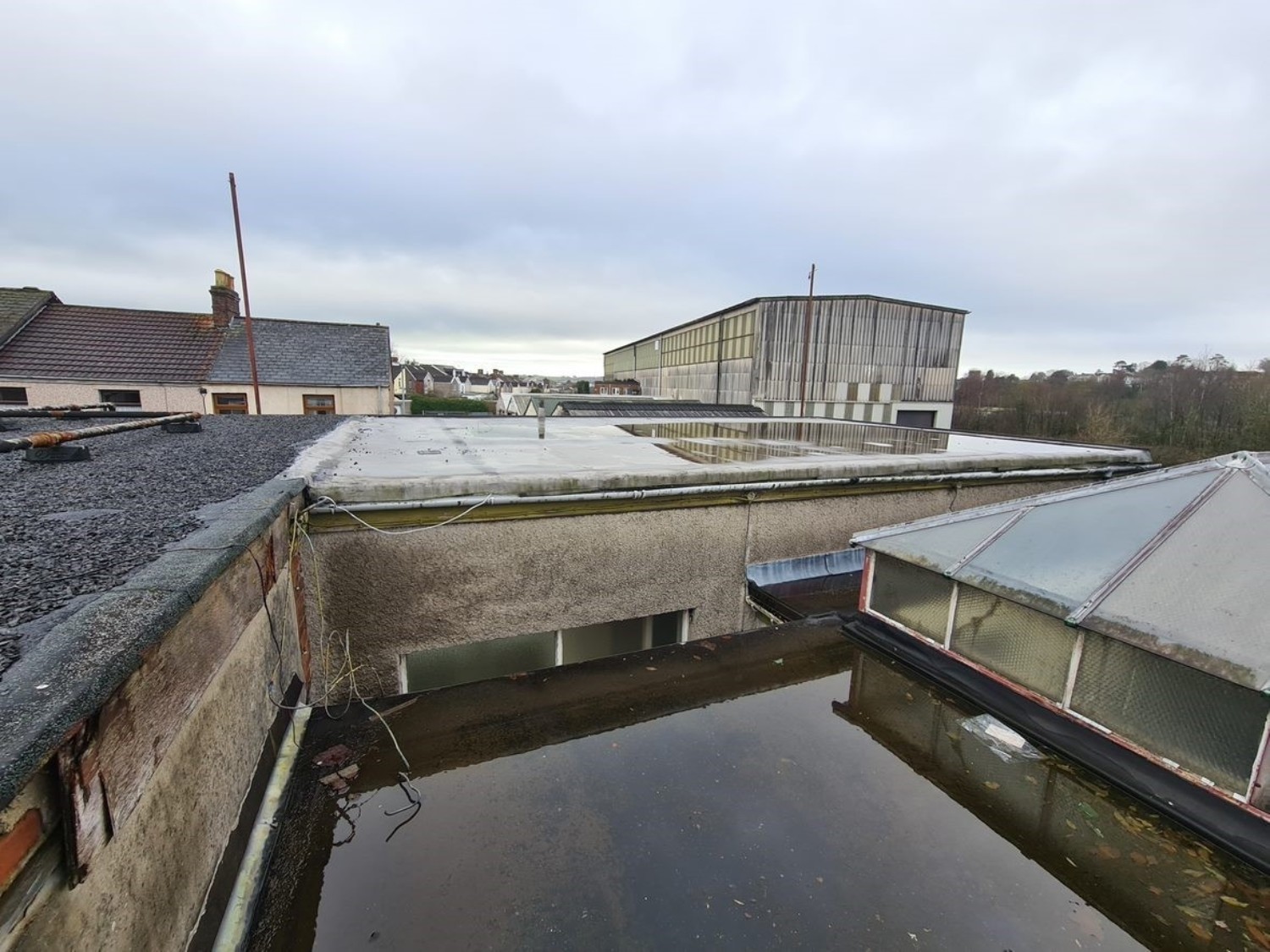 Industrial rooftop view showing concrete structures, metal cladding, and water treatment tanks under cloudy sky.