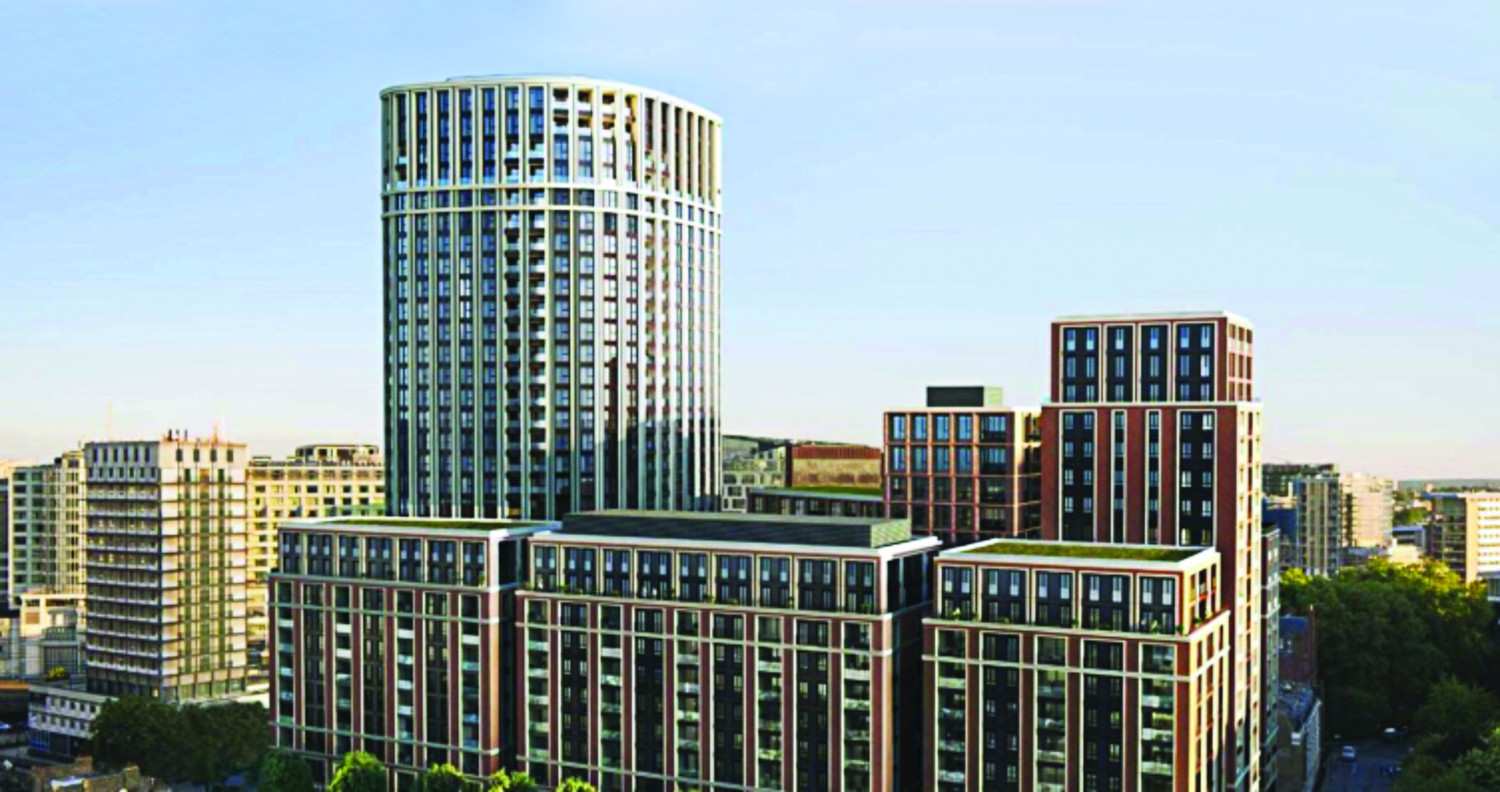 Modern mixed-use development with tall cylindrical tower and rectangular blocks featuring glass facades and colourful window panels against blue sky.
