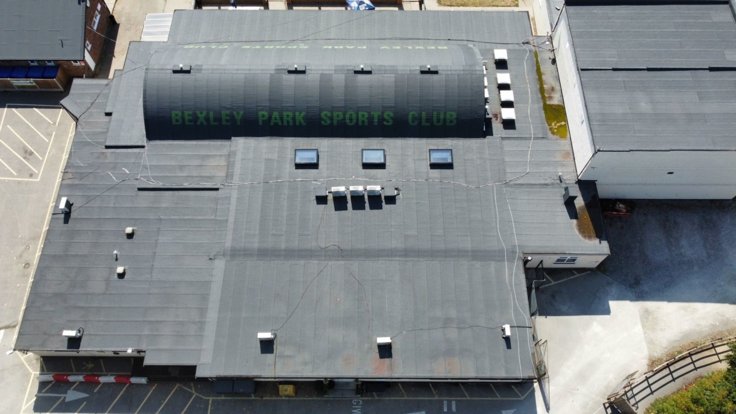 Aerial view of industrial building with grey roof featuring large green text "JOCKEY ROAD SOUTH 5AM", surrounded by concrete surfaces and adjacent structures.