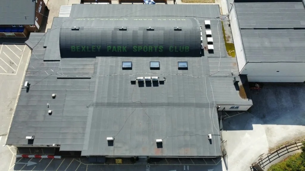 Aerial view of grey flat industrial roof with "REDEFINING RETIREMENT" text painted in dark letters, surrounded by other buildings.