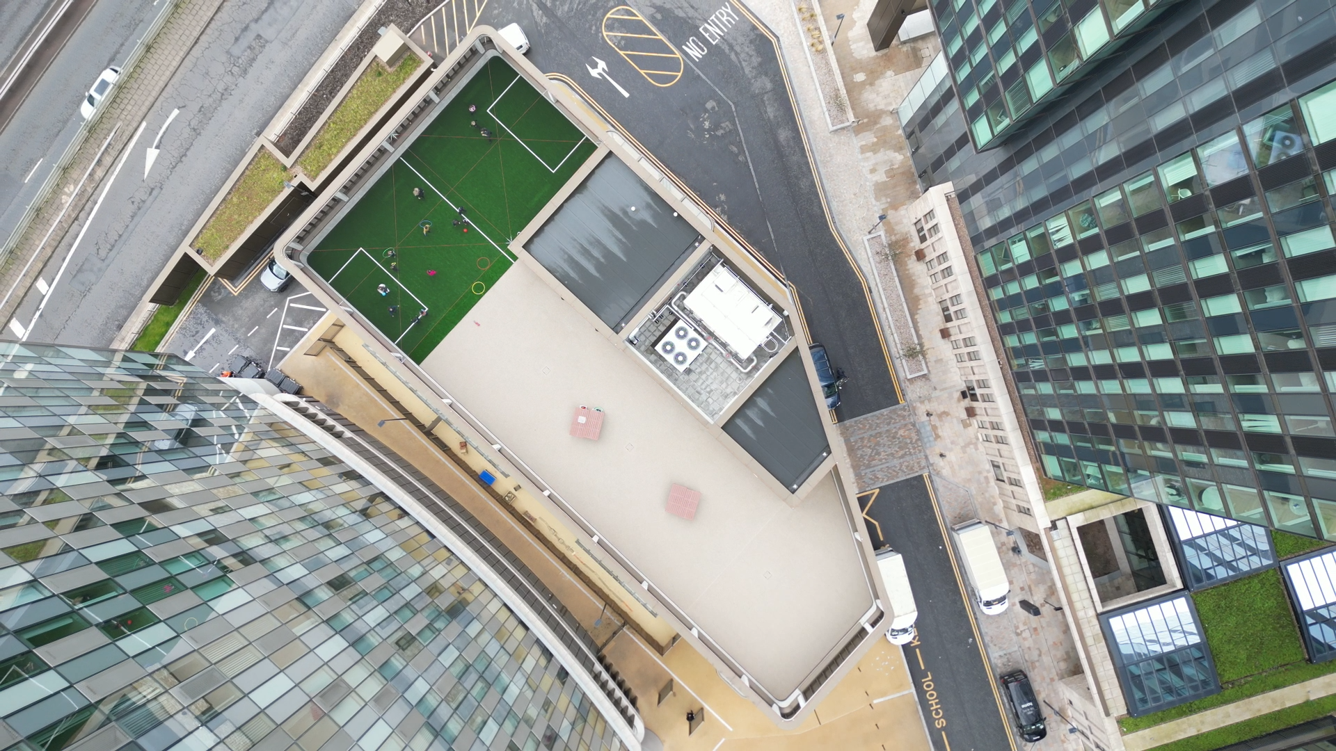 Aerial view of green football pitch surrounded by grey stadium structure, adjacent to modern glass buildings and roads.