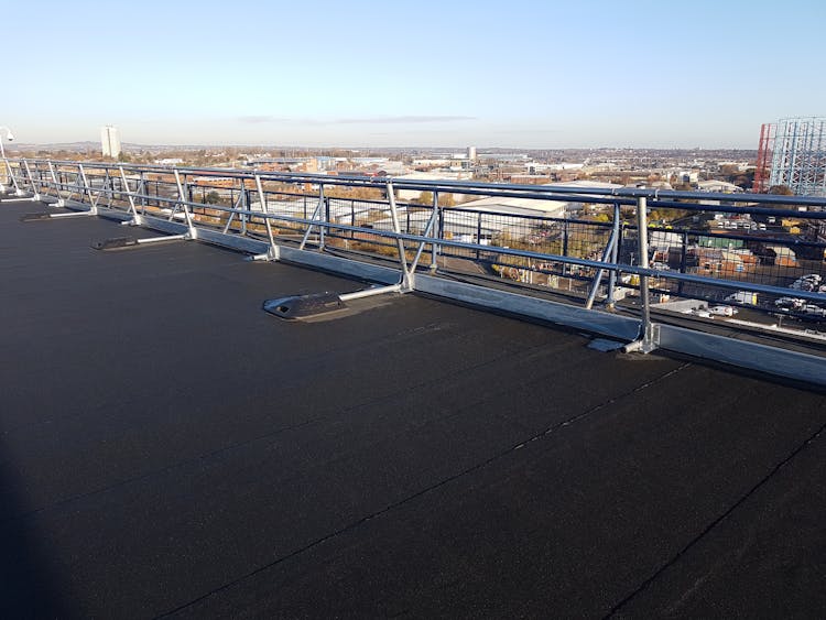 White metal safety railings on dark rooftop with industrial cityscape and pale sky in background.