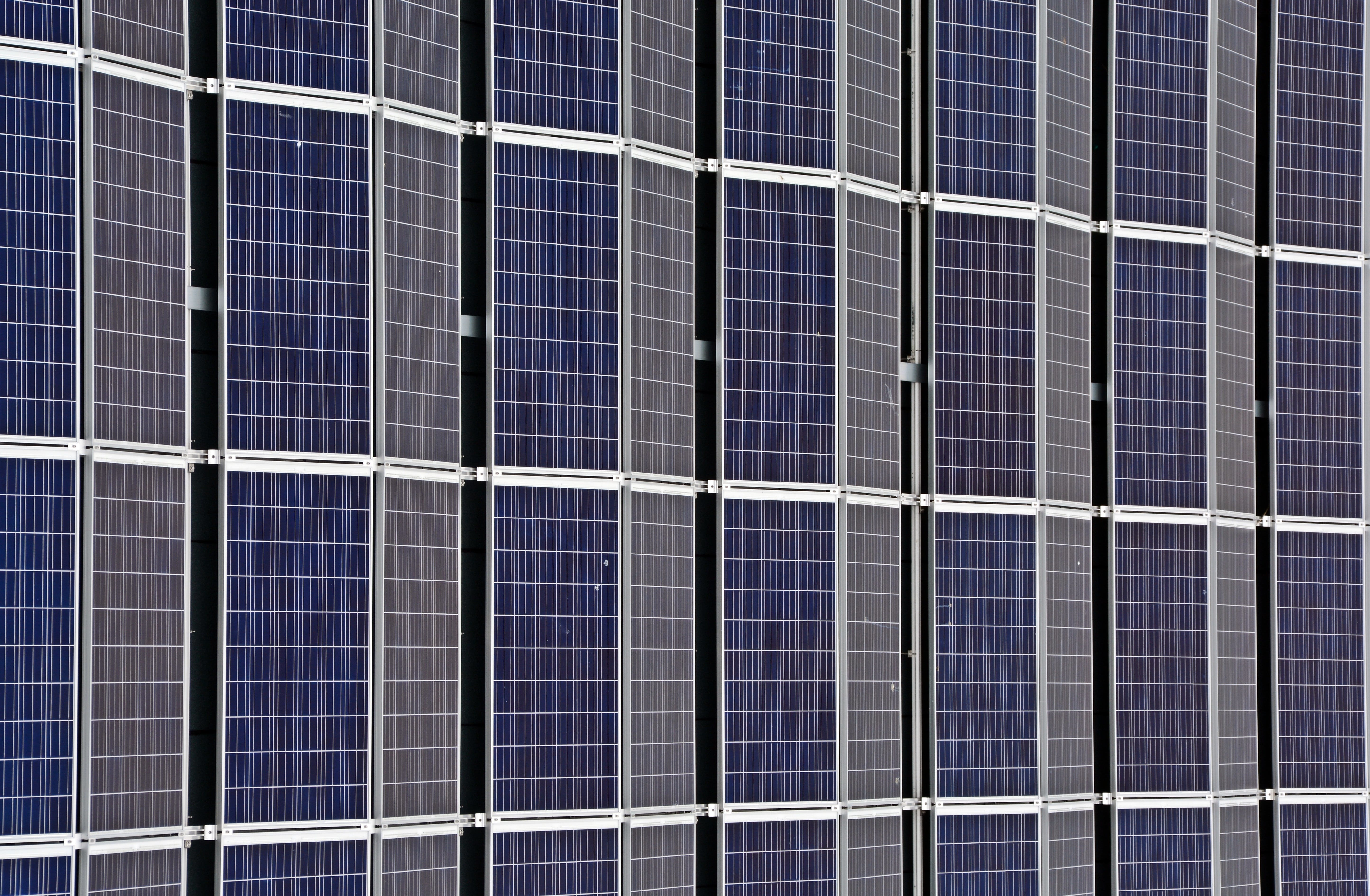 Grid of dark blue solar panels with silver metal frames and white connecting lines forming rectangular pattern.
