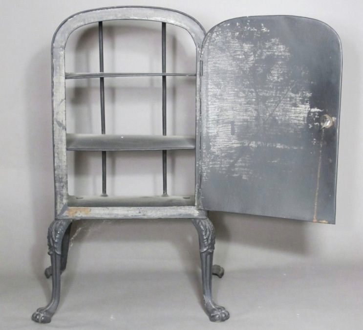 A vintage metal cabinet with lion paw feet, featuring three shelves and an open side door. Its surface has a distressed gray finish, revealing signs of wear and age.