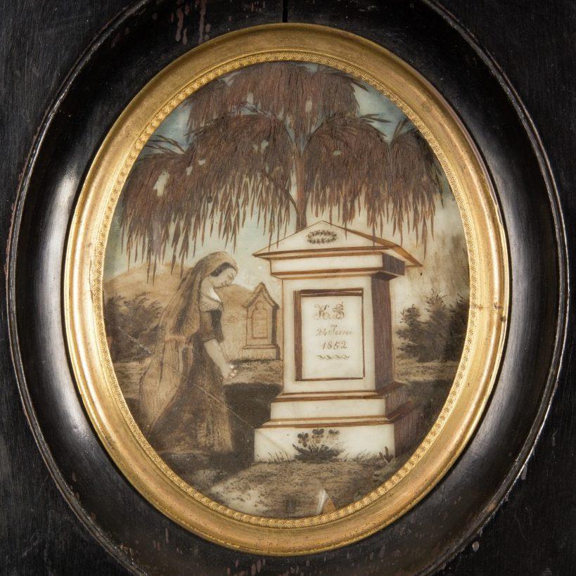 A framed oval painting depicts a woman in mourning by a grave adorned with a weeping willow tree. The headstone displays the initials K.S. and the year 1812. The background shows distant hills and a small monument.