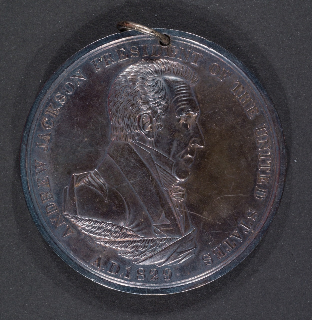 A commemorative coin featuring a side profile of Andrew Jackson with inscriptions that read Andrew Jackson, President of the United States, AD 1829. The coin also has a loop at the top for hanging or displaying.