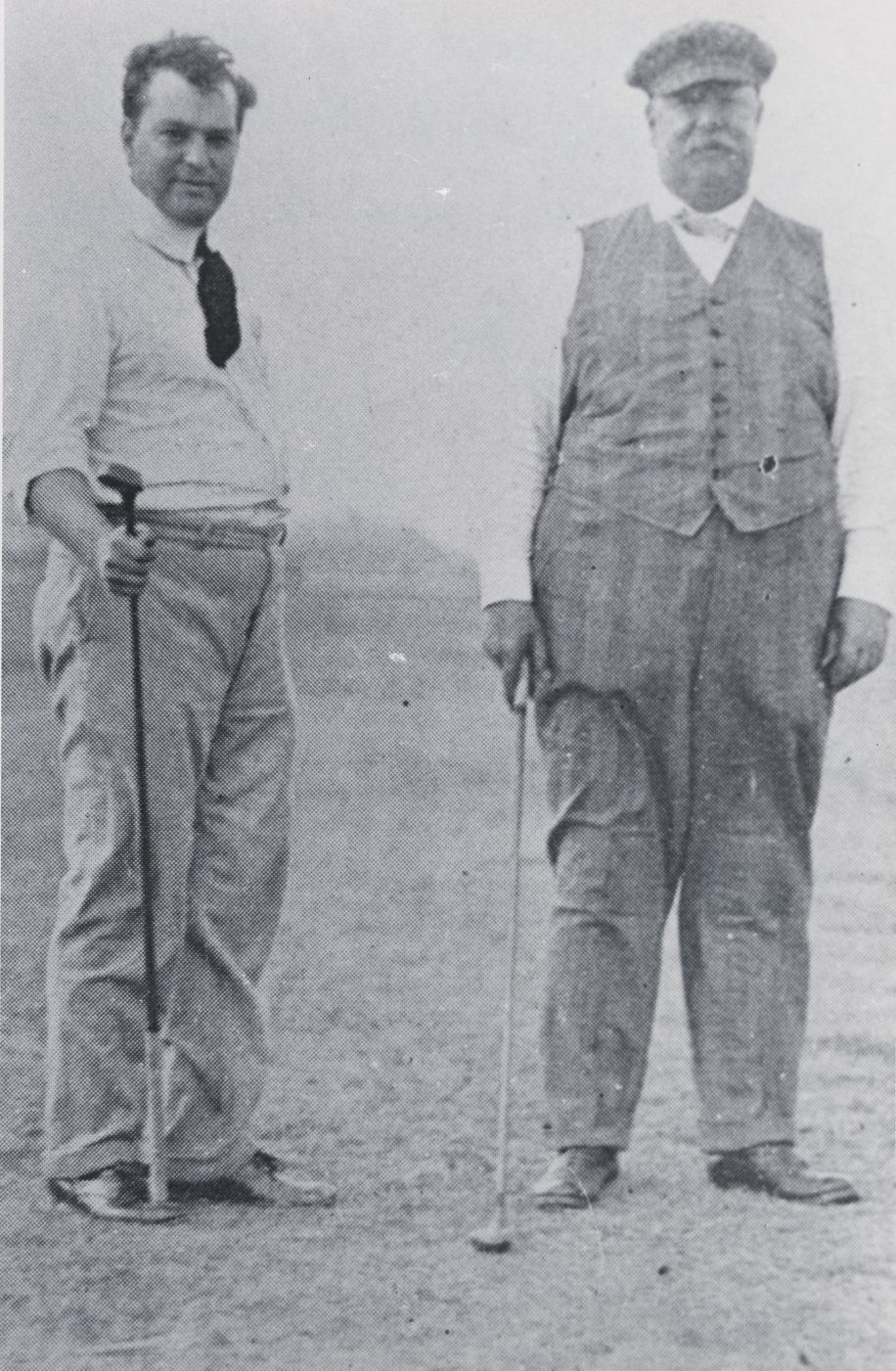 Two men in vintage attire stand on a golf course. One wears a tie and holds a golf club; the other, wearing a vest and flat cap, stands beside him with another club. The background is a misty landscape.
