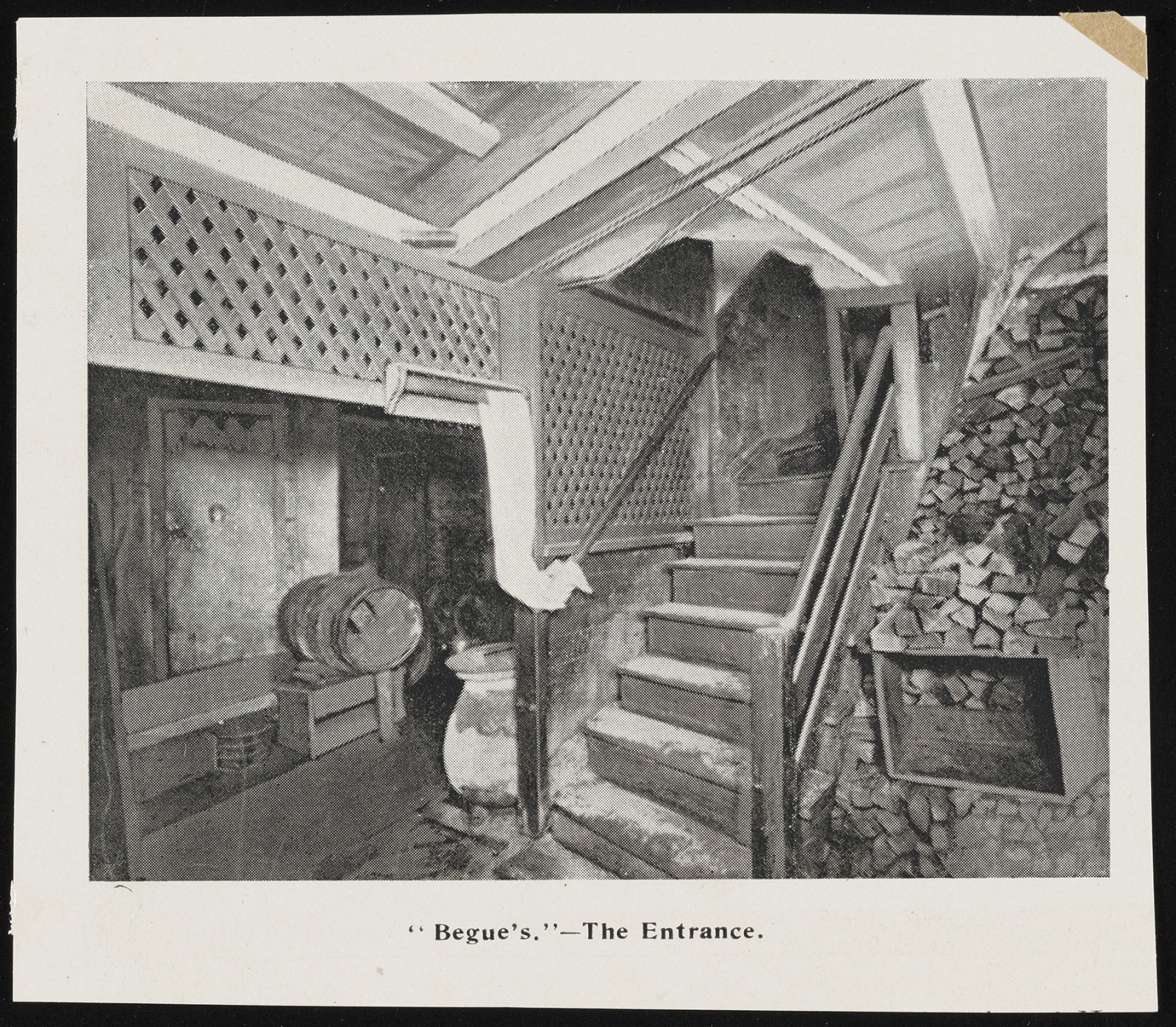 A black and white photo of an interior staircase leading down past a stack of chopped wood.