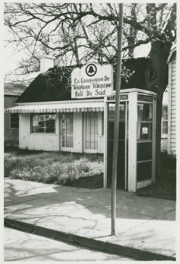 A vintage photo of a telephone booth labeled Telephone outside a small building with a sign reading La Compagnie De Telephone-Telegraphe Bell Du Sud. The building has a canopy and large windows, surrounded by trees and a sidewalk.