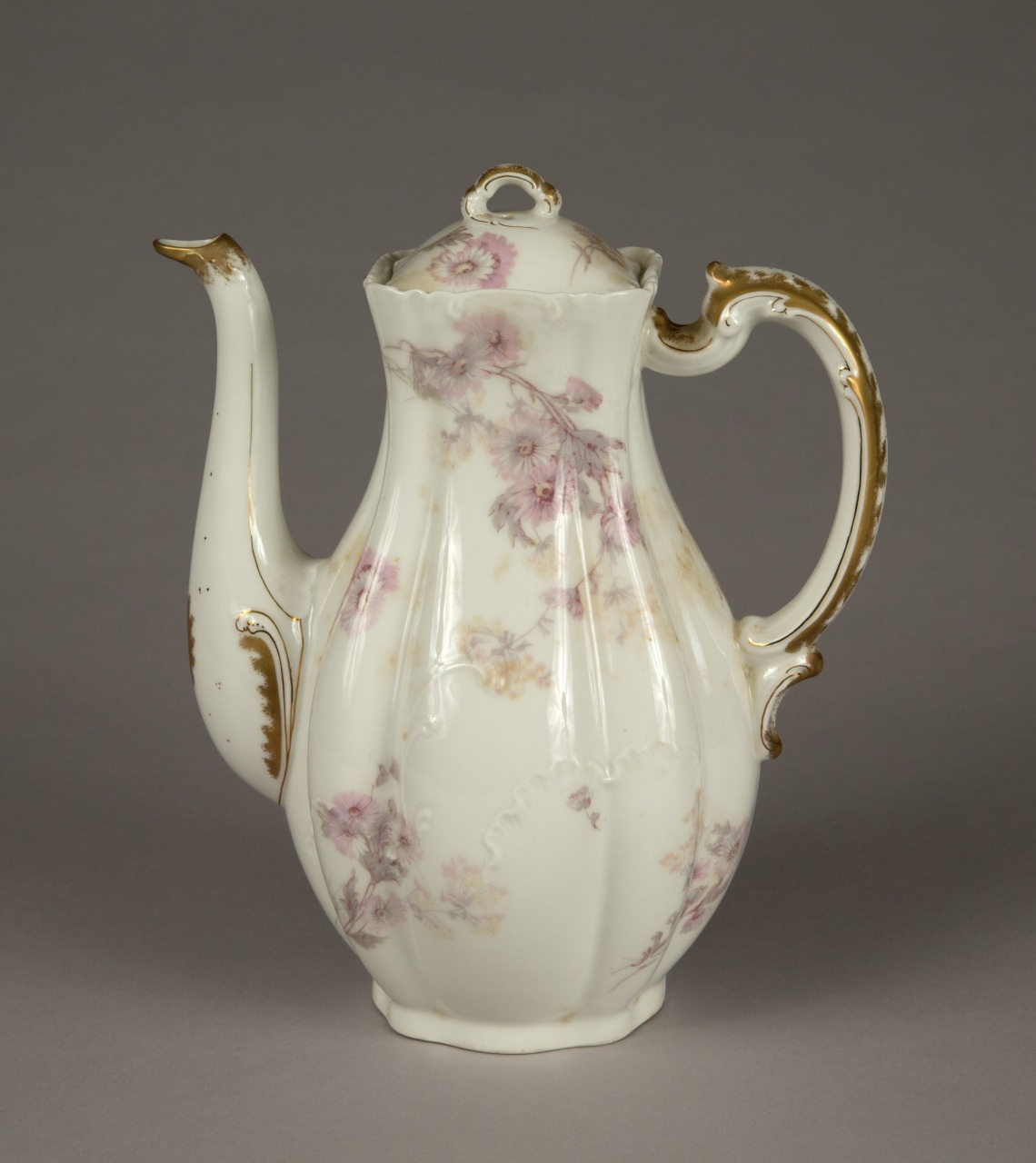 A vintage porcelain teapot with a curved spout and handle, decorated with delicate pink floral patterns and gold accents, set against a neutral gray background.