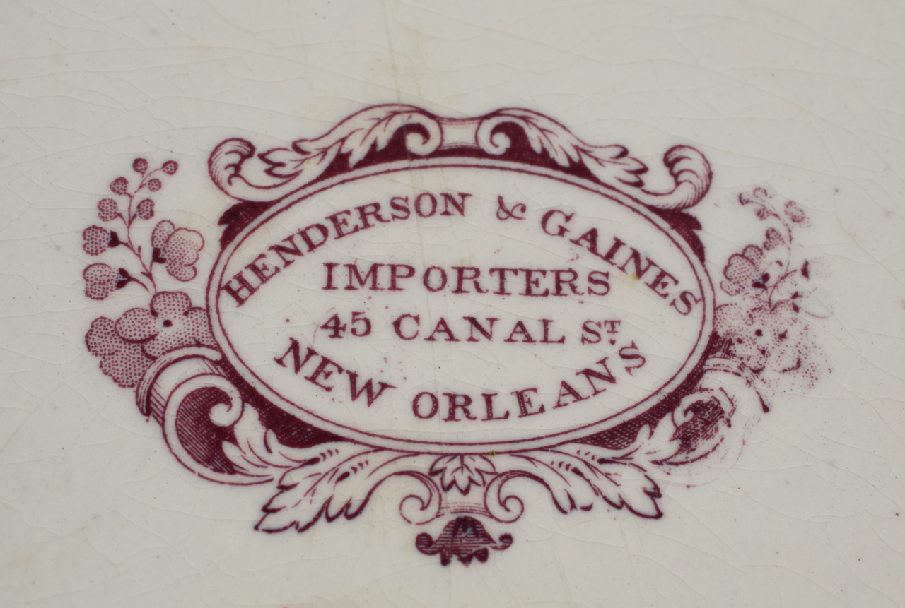 Ornate decorative logo with floral designs, stating Henderson & Gaines, Importers, 45 Canal St, New Orleans in maroon text on a white, textured background.