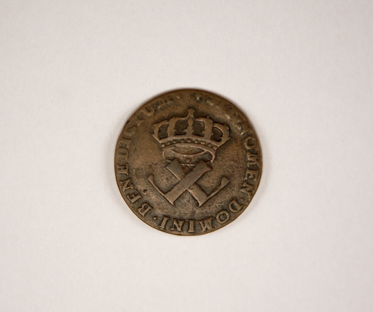 A vintage coin with a crown above crossed keys design, surrounded by the inscribed words BENEDICTVM DOMINIC, placed against a neutral background.