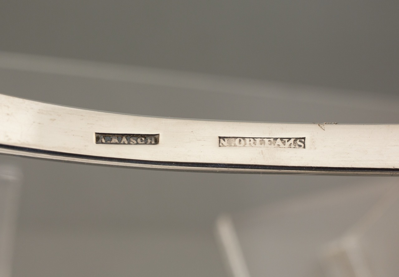 Close-up of a silver object featuring engraved hallmarks. The markings read K.A. Aasch and Norway in small, rectangular marks. The object has a smooth, shiny surface with a slight curve.