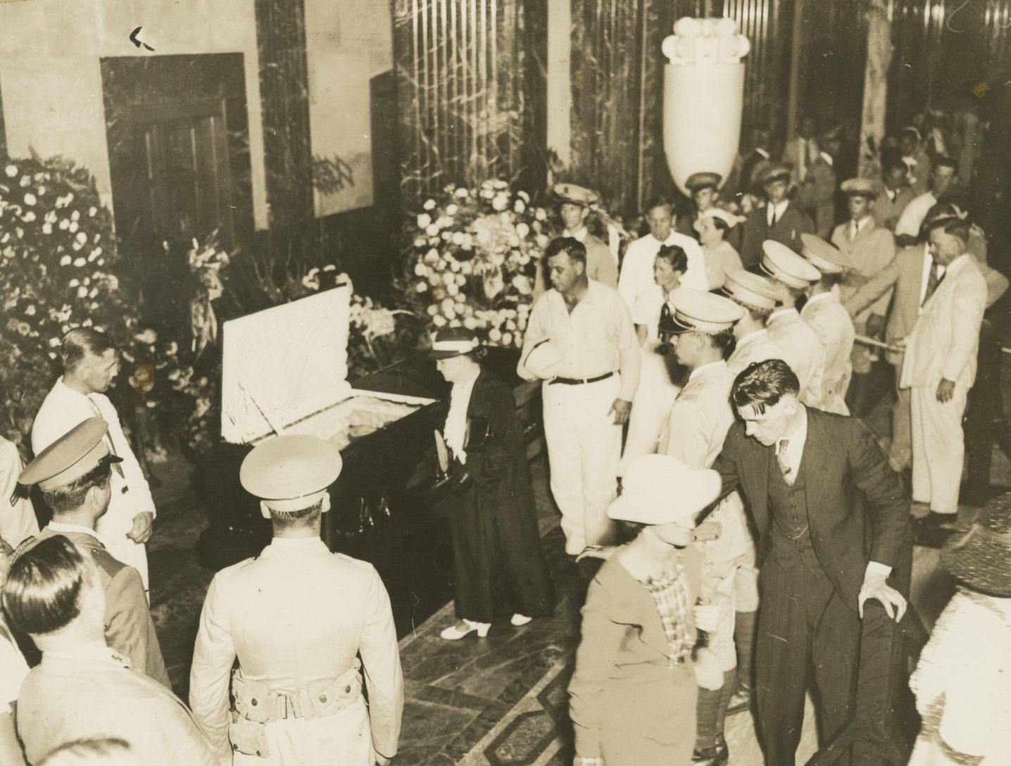 A sepia photo of mourners surrounding Huey Long's casket.