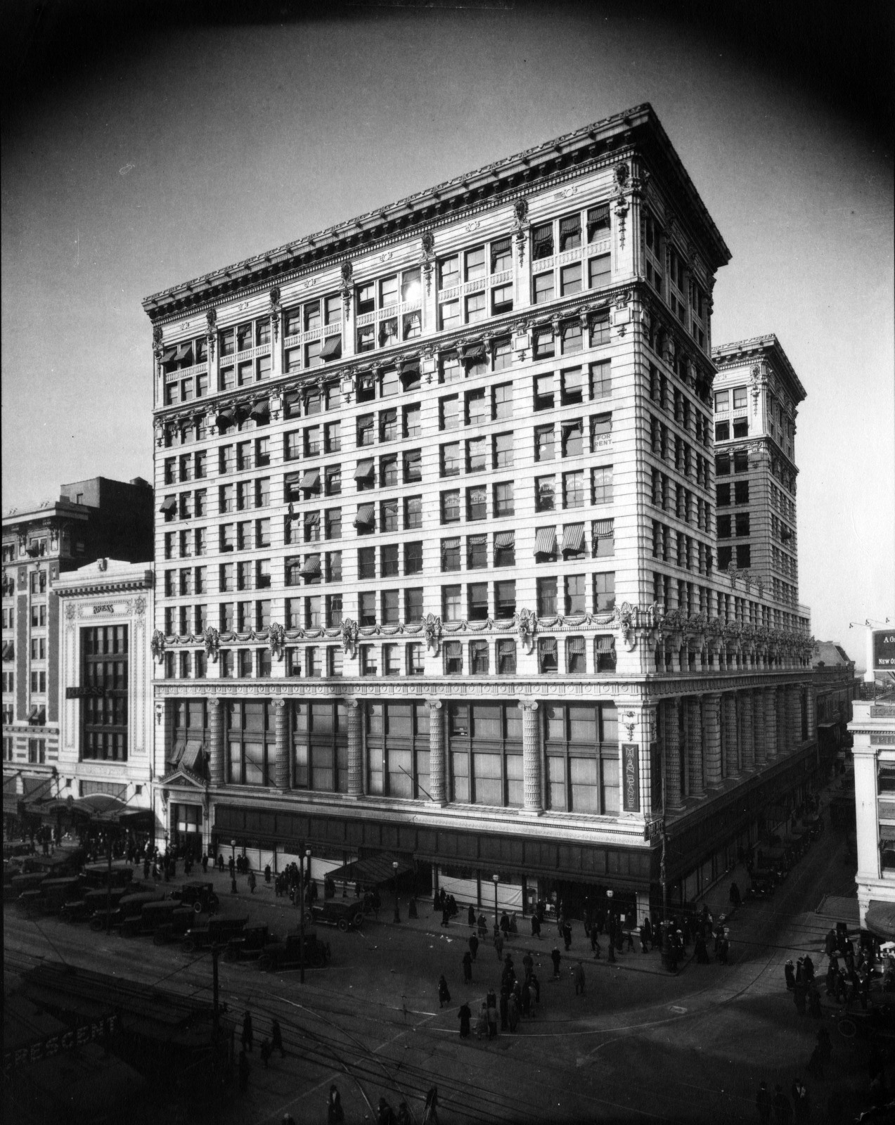 A historic black and white photograph of the Crescent Department Store building, featuring ornate architectural details and multiple stories. The streets below are bustling with pedestrians, cars, and streetcars under a clear sky.