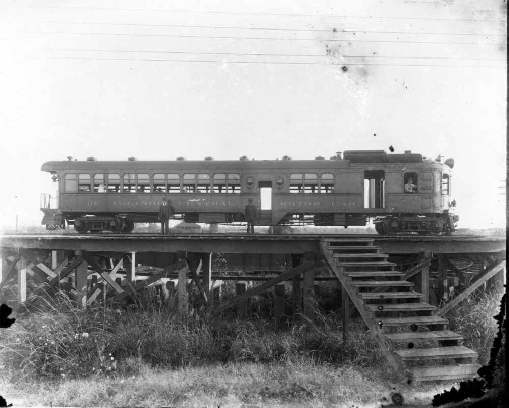 A vintage black and white photograph of a single trolley car on elevated tracks. The side of the trolley reads THE ILLINOIS TRACTION SYSTEM. There are stairs leading up to the tracks in the foreground, with grass below.