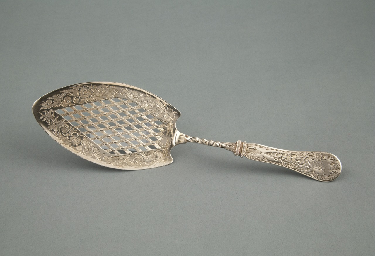 An ornate silver slotted serving utensil with intricate floral engravings on the handle and around the slotted section, set against a plain background.