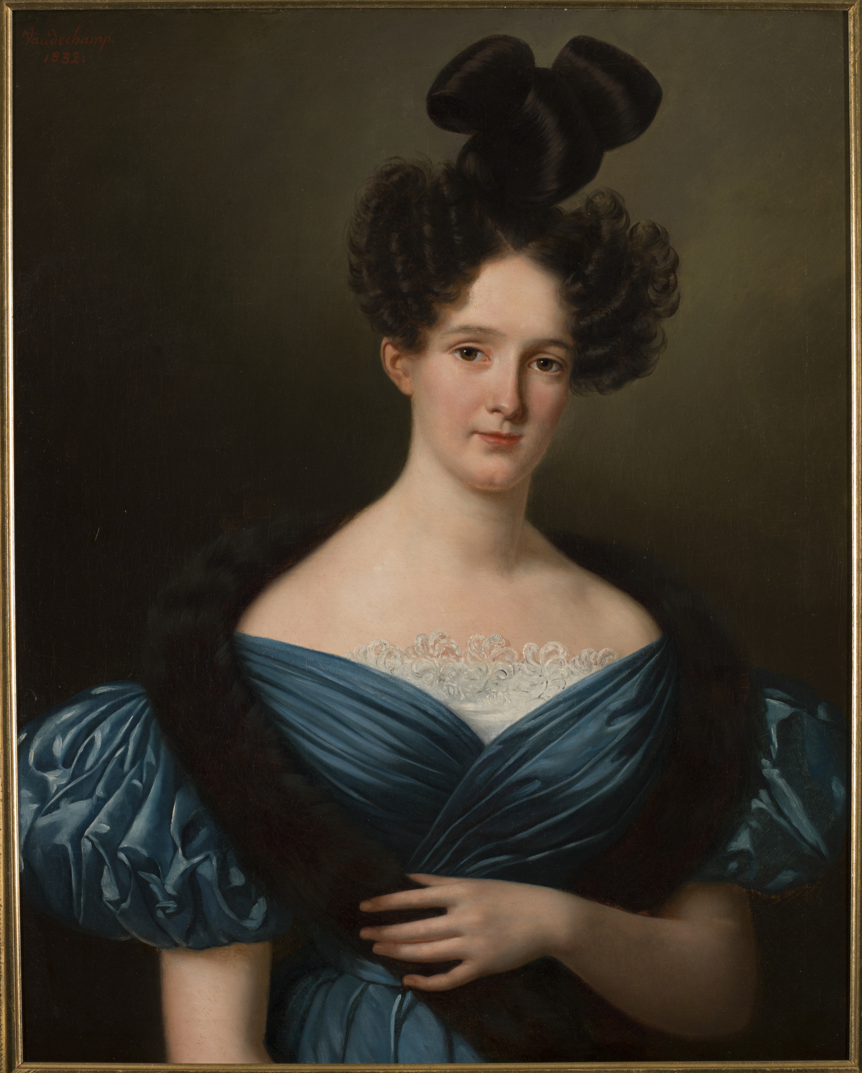 A classic portrait of a woman in period clothing, wearing a blue dress with lace details and a dark fur stole. She has an elaborate hairstyle with a large bow on top. The backdrop is a plain, dark background.
