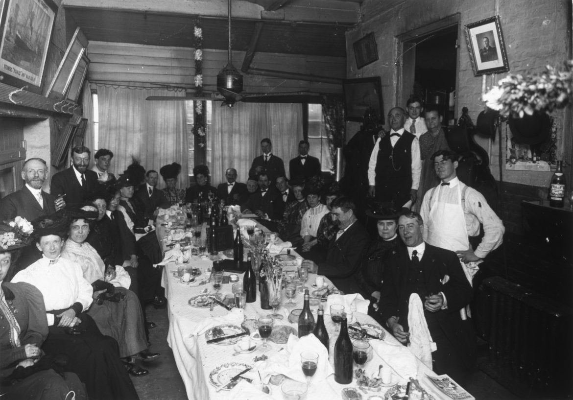 A very full Begue's dining table lined with well-dressed diners smiles for the camera.