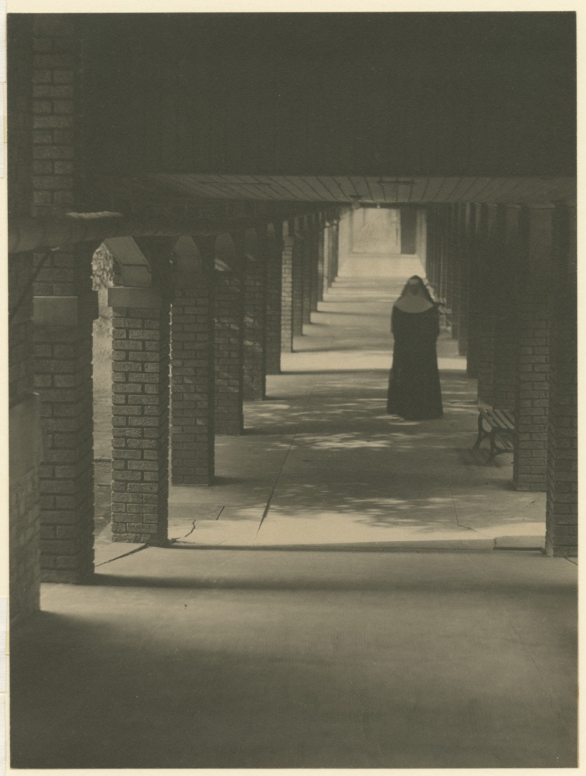 A vintage sepia-tone photograph shows a nun walking among brick columns at the Ursuline Convent circa 1930.