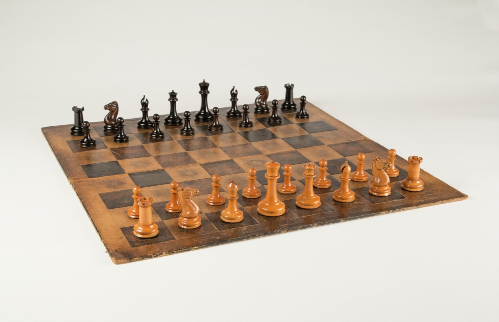 A vintage chessboard with a complete set of light and dark wooden chess pieces arranged for the start of a game. The board has a worn, rustic appearance against a plain background.