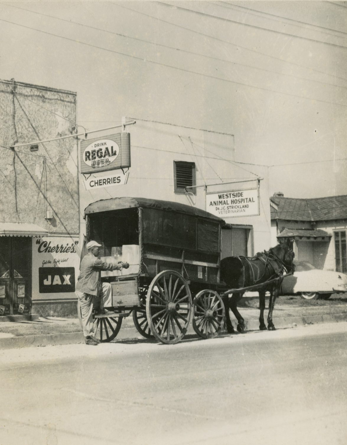 An iceman reaches for a large block of ice in the back of his horse-drawn carriage.