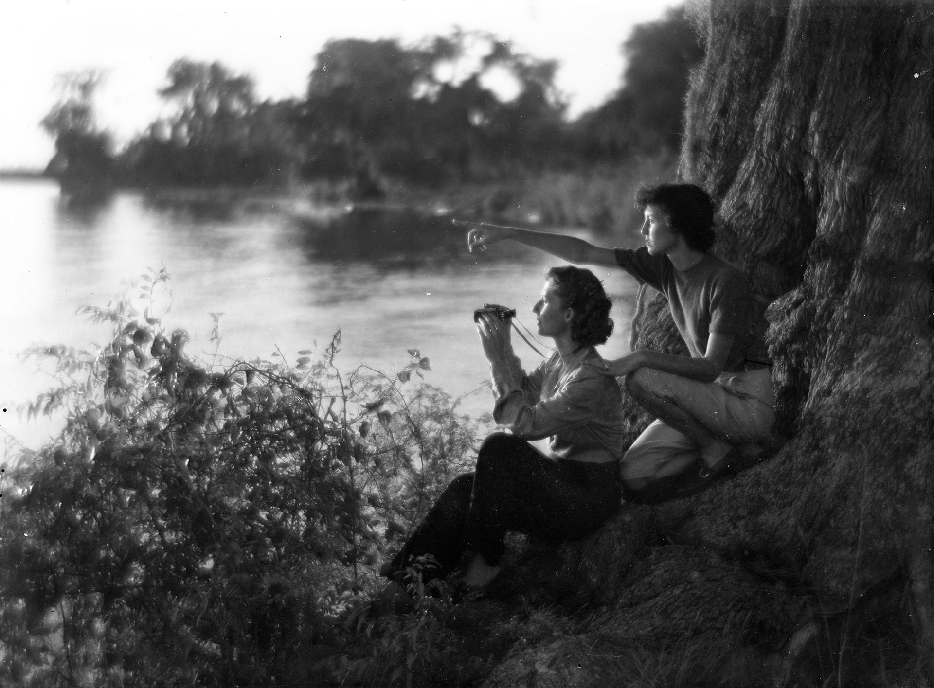 A black and whit ephoto of two women seated near a Louisiana waterway with binoculars.