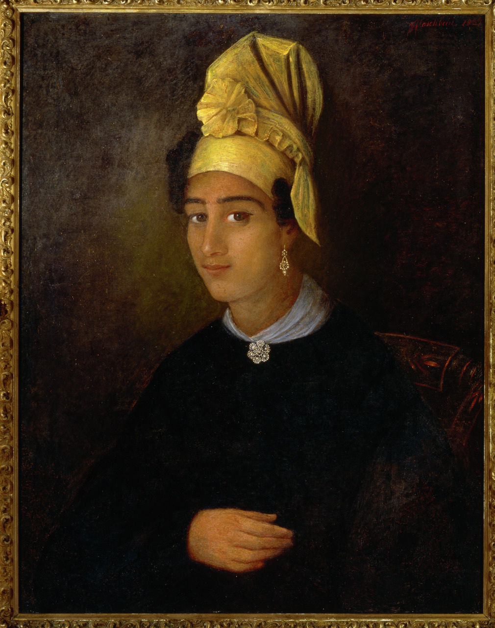 A portrait of a person wearing a large yellow turban adorned with a flower, earrings, and a brooch on their dark garment. They are sitting against a dark background, framed in an ornate gold frame. The painting style is classic and detailed.