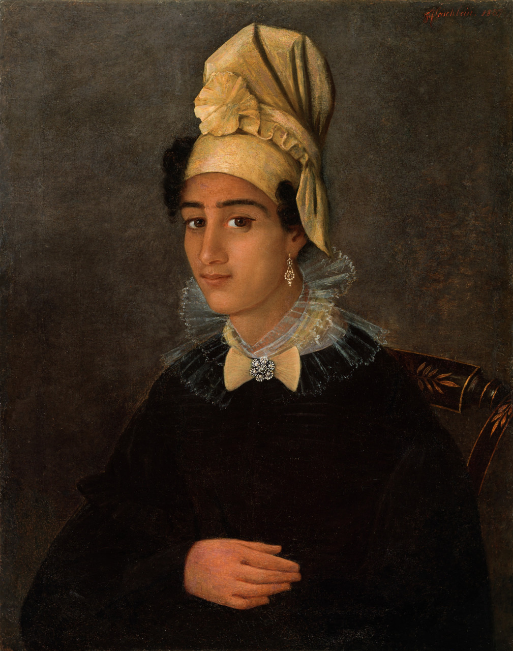 A portrait of a person wearing a dark outfit with lace trim, a cream headscarf, and a jeweled earring. The individual is seated against a plain background, looking at the viewer with a composed expression.
